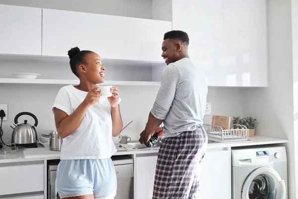 Um trabalho de amor. Tiro de um jovem lavando a louça enquanto sua esposa toma uma xícara de café em casa. — Fotografia de Stock