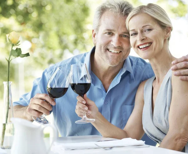 Masih cinta dan berkomitmen satu sama lain. Pasangan yang bahagia dan dewasa bersulang untuk cinta mereka dengan dua gelas anggur sementara di luar ruangan. — Stok Foto