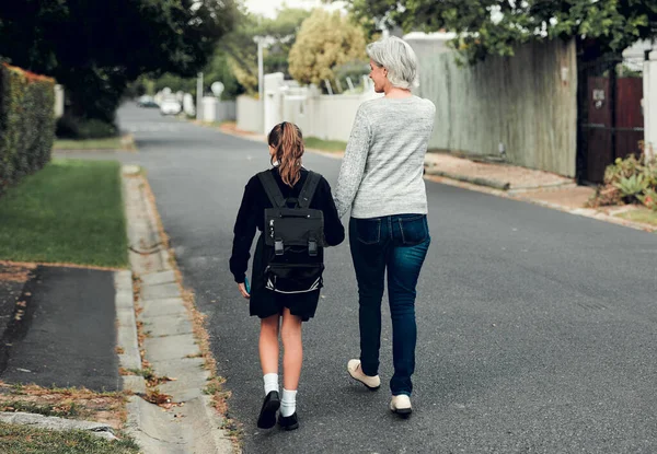 去学习新的东西。一个年轻的女学生和她的祖母一起在邻居家的大街上步行上学的全景照片. — 图库照片