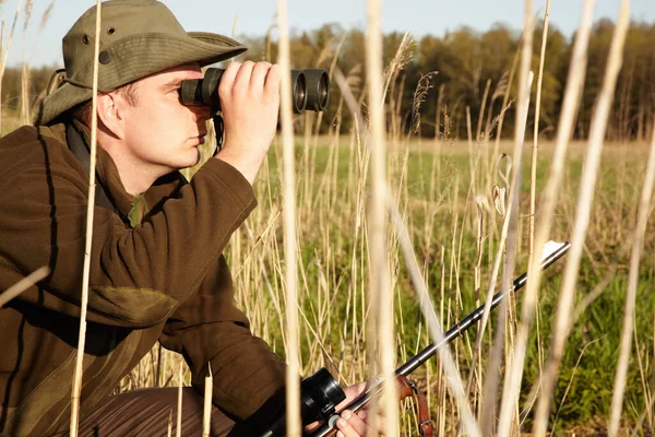 Bij nader inzien. Een man in het wild kijkt door zijn verrekijker met zijn geweer.. — Stockfoto