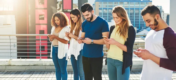 Este é o mundo em que vivemos agora. Tiro recortado de um grupo de jovens mensagens de texto em seus celulares enquanto estão de pé ao ar livre. — Fotografia de Stock