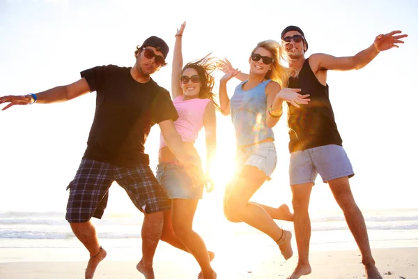Moge je schoenen gevuld zijn met zand. Opname van een groep vrienden die bij zonsondergang langs een strand lopen. — Stockfoto