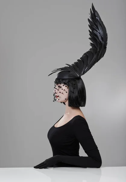 Soaring to new heights in fashion. Shot of a young woman in a wing-shaped headpiece sitting in a studio. — Stock Photo, Image