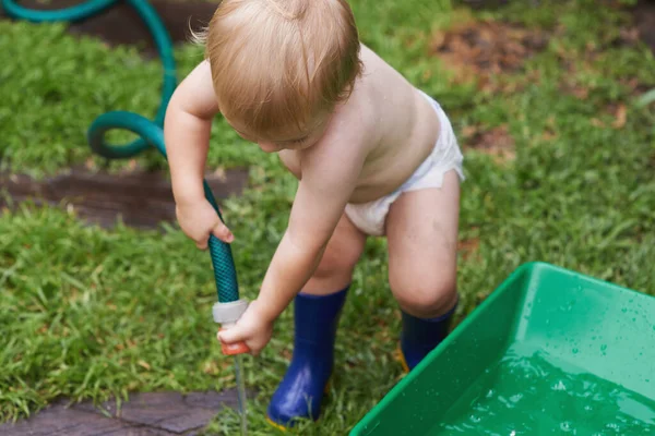 Divirtiéndome en mi nueva aventura. Un niño en su pañal y botas de goma regando el jardín. —  Fotos de Stock