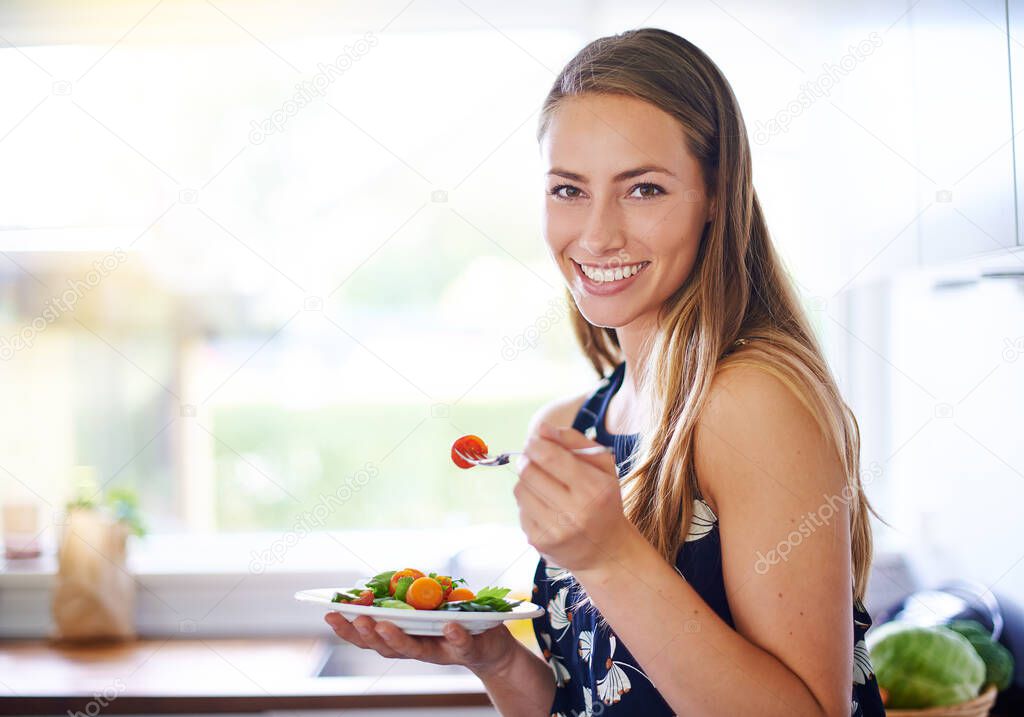 Eat healthy to live healthy. Portrait of a young woman eating a bowl of strawberries at home.