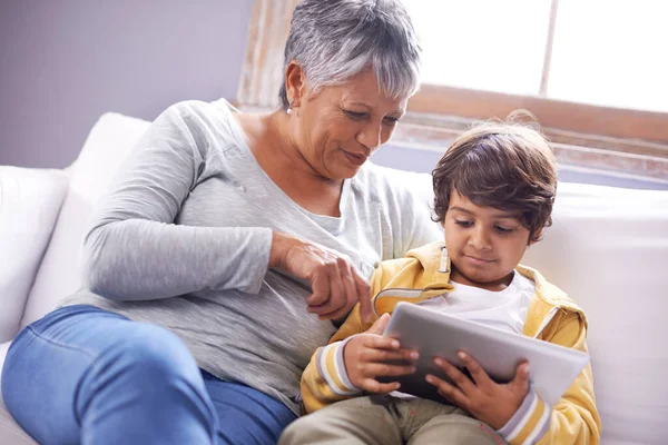 Megleckéztetem a nagyit a neten. Egy nagymama és unokája, amint otthon ülnek egy digitális táblagéppel.. — Stock Fotó