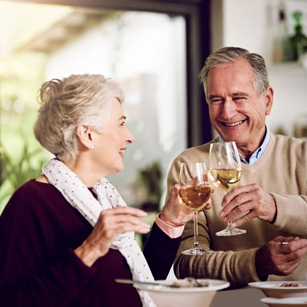 Ze proosten op hun gouden jaren. Schot van een bejaard echtpaar dat samen thuis van een maaltijd en wijn geniet. — Stockfoto