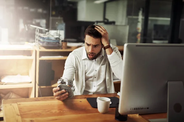 Só faltam horas por dia. Tiro de um belo jovem empresário segurando um despertador e olhando estressado enquanto trabalhava até tarde em um escritório. — Fotografia de Stock