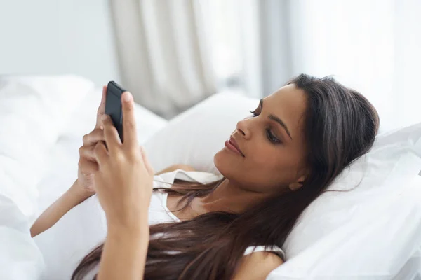 Primer texto del día. Foto de una hermosa joven que se relaja en la cama con su teléfono móvil. —  Fotos de Stock