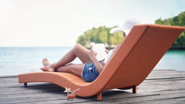 É assim que se parece o relaxamento total. Tiro de comprimento total de uma jovem atraente sentada em uma espreguiçadeira e lendo um livro durante as férias. — Fotografia de Stock