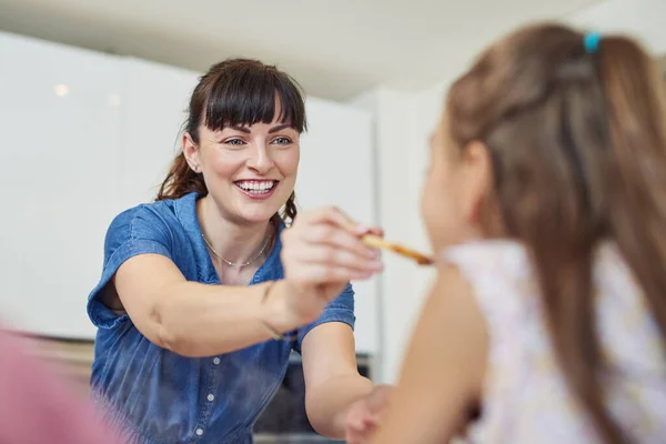 Fiz o teu favorito. Tiro de uma mãe dando a sua filha um sabor da refeição que ela cozinha em casa. — Fotografia de Stock