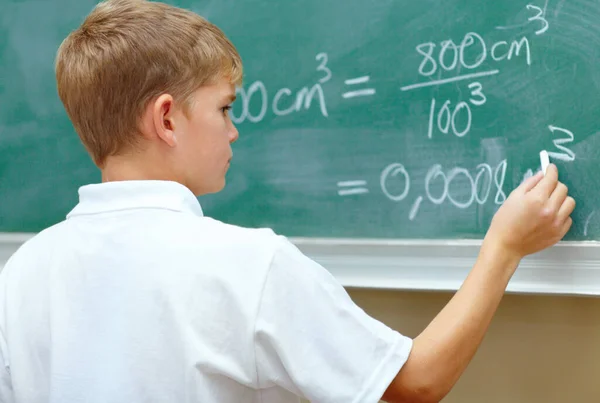 Han är ett ungt geni. Ung skolpojke gör en ekvation på svarta tavlan i skolan. — Stockfoto