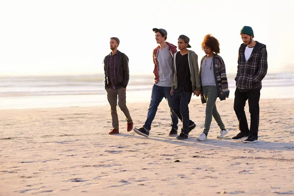 Omarm rust. Opname van een groep vrienden die bij zonsondergang langs een strand lopen. — Stockfoto