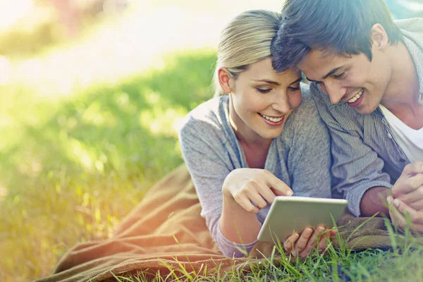 뒷마당에서 둘러보고 있어. 풀밭에 누워 디지털 태블릿을 함께 사용하는 행복 한 젊은 부부의 사진. — 스톡 사진