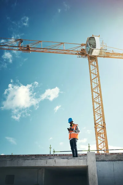 Actualización de los planes del proyecto sobre la marcha. Fotografía de un joven usando un teléfono inteligente mientras trabajaba en una obra de construcción. — Foto de Stock