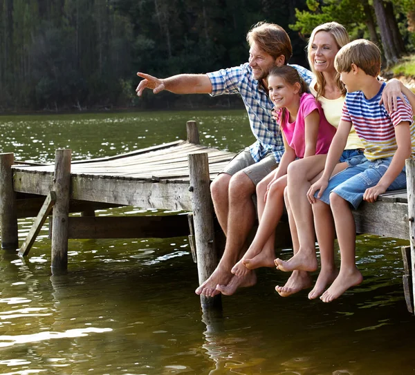 Ik bekijk het landschap. Shot van een liefdevolle familie zittend op een pier op een meer op het platteland. — Stockfoto