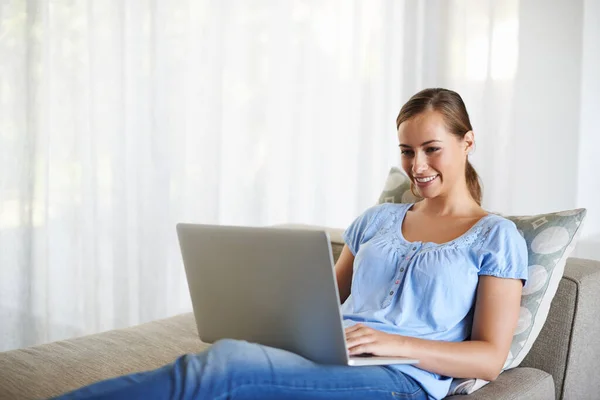 Kontroluji nejnovější aktualizace. Snímek atraktivní mladé ženy pomocí notebooku v pohodlné poloze na pohovce. — Stock fotografie