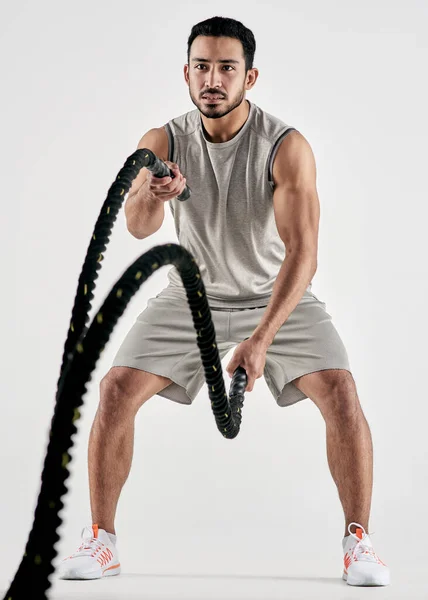 Anche nel mio peggior giorno, sto andando alla grande. Studio shot di un giovane muscoloso che si esercita con corde da battaglia su uno sfondo bianco. — Foto Stock