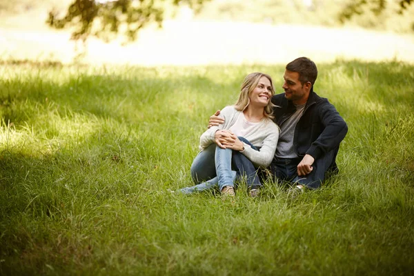 Genieten van een moment weg van dit alles. Shot van een liefdevol jong paar zittend op het gras in een park. — Stockfoto