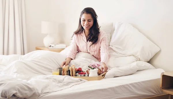 Fordi enhver kvinde fortjener morgenmad på sengen. Et billede af en smuk ung kvinde, der spiser morgenmad i sengen derhjemme. - Stock-foto
