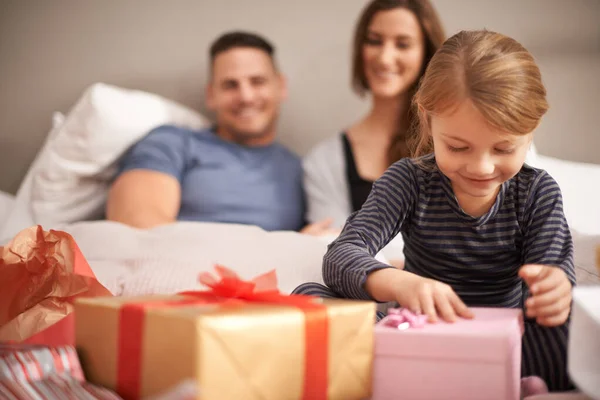 I wonder what it could be.... Shot of a little girl receiving presents in bed from her parents. — Stock Photo, Image