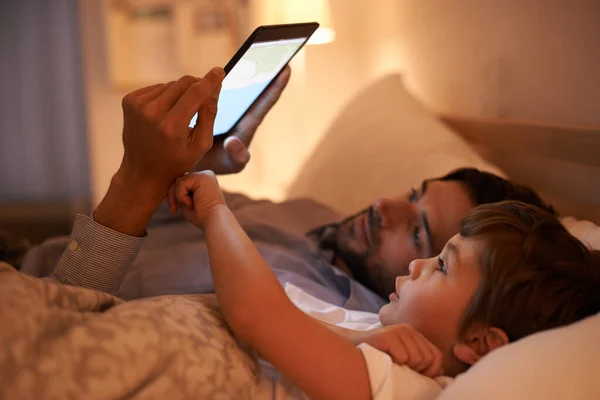 Modern verhaaltje voor het slapen gaan. Een vader die een verhaaltje voorleest aan zijn zoon uit een e-reader. — Stockfoto