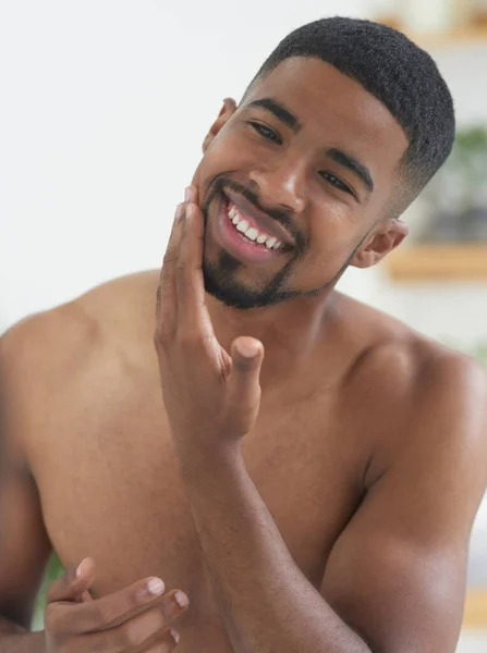 İşin sırrı tıraş losyonunda. Genç ve yakışıklı bir adamın banyodaki cildine tıraş losyonu sürerken görüntüsü.. — Stok fotoğraf