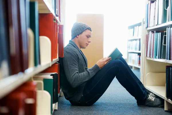 Obtenir son matériel d'étude pour l'année. Un jeune homme assis par terre et lisant dans une bibliothèque. — Photo