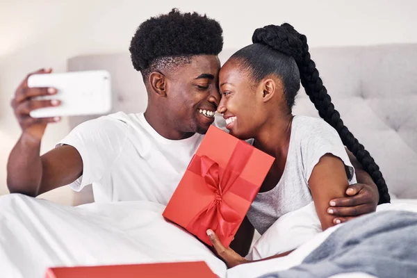 Quiero capturar este momento. Fotografía de una mujer joven sosteniendo una caja de regalo mientras se toma una selfie con su novio. — Foto de Stock