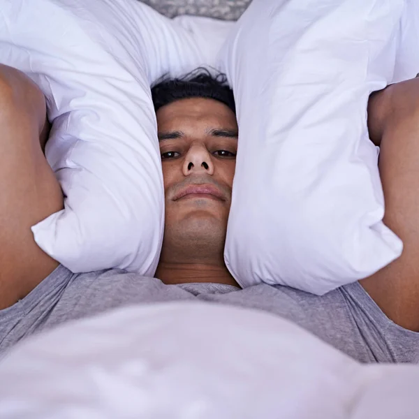 Nadie puede dormir con todo este ruido. Un joven cubriéndose las orejas con su almohada. — Foto de Stock
