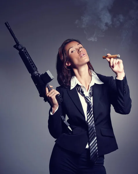 Вверх у дим. Молода бізнес-леді в костюмі і краватці тримає гвинтівку під час куріння сигари . — стокове фото