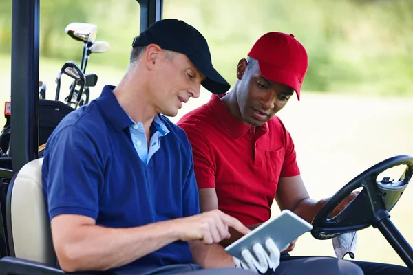 Obtenir les meilleurs conseils de golf en ligne. Tourné de deux hommes dans une voiturette de golf regardant une tablette numérique. — Photo