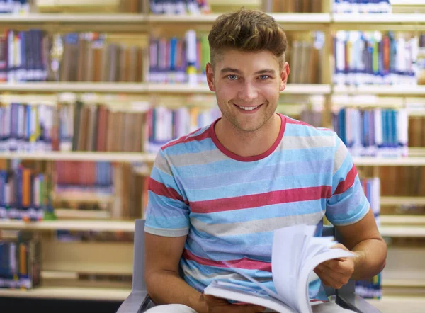 Hitta en lugn plats att studera på. Porträtt av en stilig ung collegestudent som studerar i biblioteket. — Stockfoto