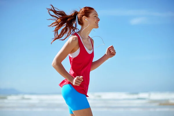 Music motivates her. Cropped shot of a young woman running on the beach. — Stock Photo, Image