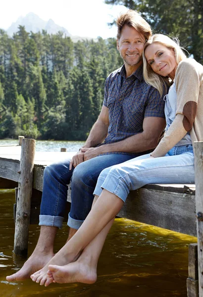 Alltid komfortabel i hverandres selskap. Skutt av et kjærlig modent par som satt på en brygge ute på en sjø på landet. – stockfoto
