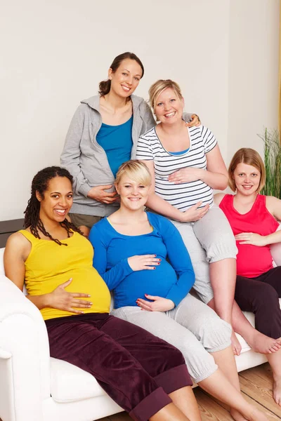 We kunnen niet wachten op de grote dag. Een groep multi-etnische zwangere vrouwen zit op een bank en glimlacht naar de camera. — Stockfoto