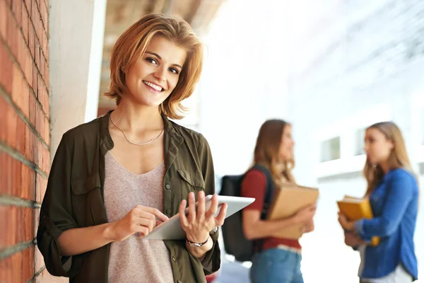 Technology is helping me excel at college. Portrait of a smiling female university student standing on campus using a digital tablet with friends in the background. — Stock Photo, Image