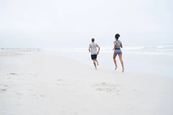 Przygotowują swoje ciała na lato. Zdjęcie z tyłu młodej pary biegającej razem po plaży. — Zdjęcie stockowe