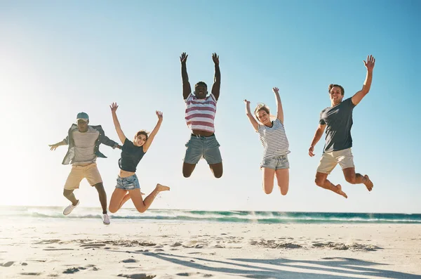 Bryt deg løs med dine beste venner. Skutt av en gruppe unge venner som hoppet entusiastisk opp i luften på stranden. – stockfoto