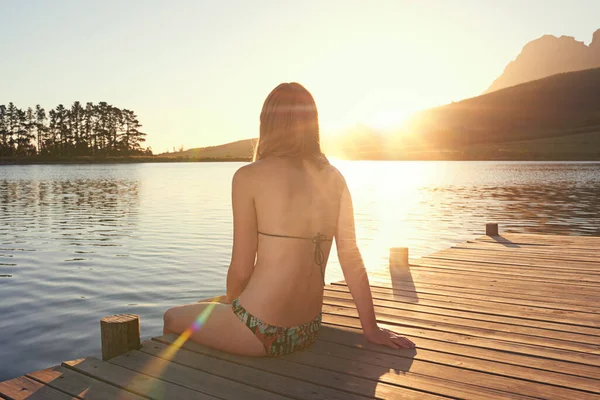 日没時の湖。夕暮れ時に湖のそばのドックに座っているビキニの若い女性のショット. — ストック写真