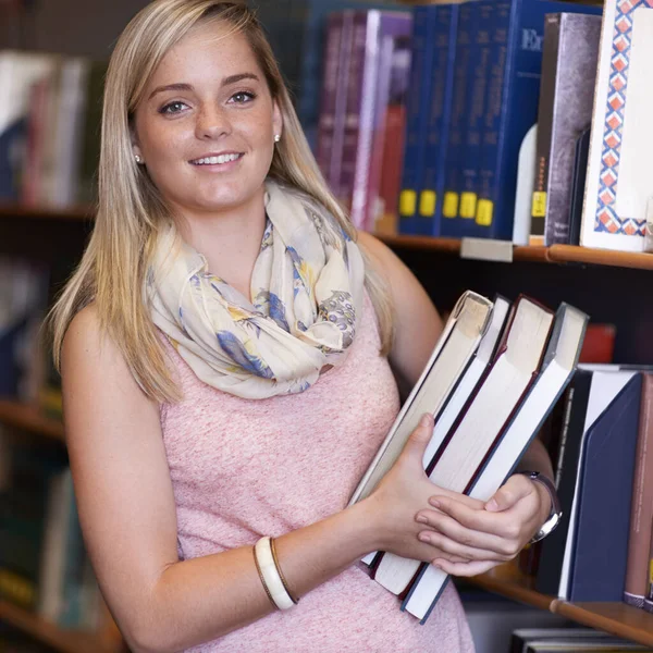 Hon är en riktig bokmal. En ung kvinna får böcker från en bibliotekshylla. — Stockfoto