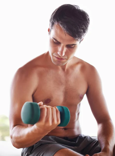 En serio sobre la aptitud. Un joven musculoso sentado y levantando pesas en casa. —  Fotos de Stock