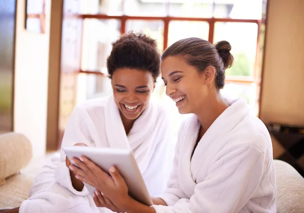 Registrarse en el spa. Toma de dos amigos en albornoces usando una tableta digital en un spa. — Foto de Stock