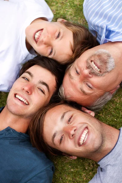 Сміються разом протягом століть. Батько і сини лежать на траві з головами один біля одного . — стокове фото