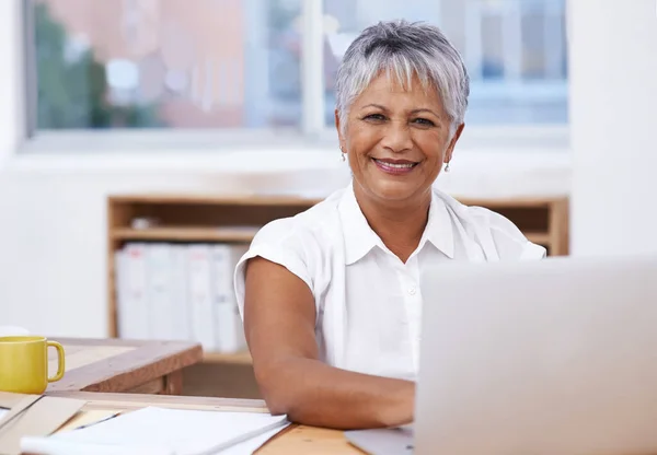 Ella es la fuerza impulsora detrás del éxito de la compañía. Retrato de una mujer de negocios madura usando su computadora portátil mientras está sentada en su escritorio. — Foto de Stock