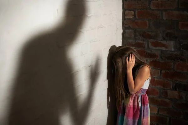 Wehrloses Opfer. Misshandeltes kleines Mädchen zusammengekauert, während der Schatten ihres Täters auf sie zukommt. — Stockfoto