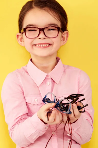 Olha quantos eu tenho. Uma menina bonita de pé contra um fundo amarelo com uma mão cheia de óculos. — Fotografia de Stock