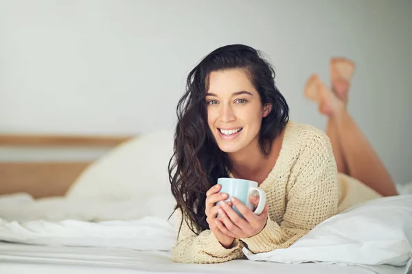 週末に私の方法を緩和します。ベッドの上に横になりながらコーヒーを飲む若い女性の完全な長さの肖像画. — ストック写真