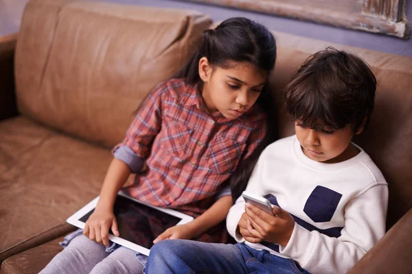 On joue avec la technologie. Tournage de deux frères et sœurs jouant avec leurs appareils numériques à la maison. — Photo