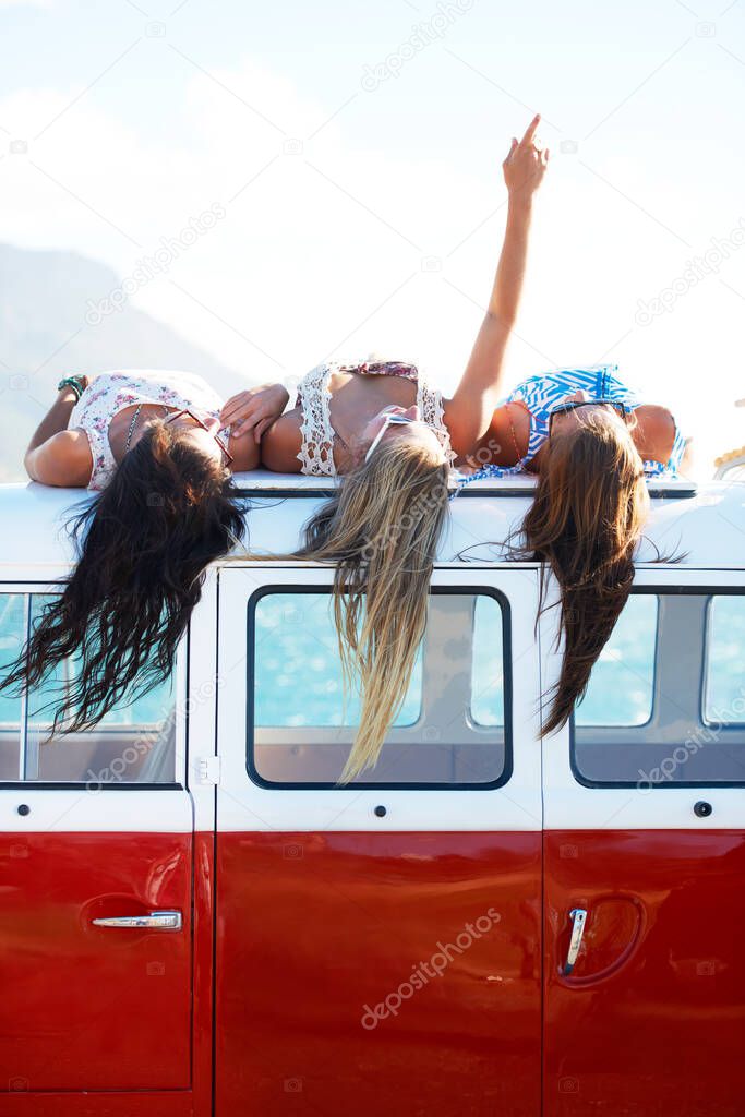 Appreciating the finer things in life. Three young girls rest on top of their van looking at the sky - copyspace.
